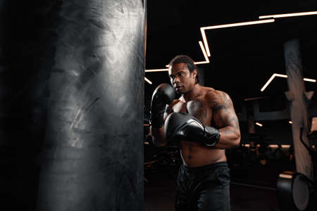 An African American guy trains in gym and fists his boxing bag fists. Concept of: gym, fitness, boxing, success, workout and powerの写真素材