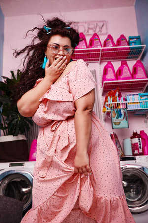 Young stylish plus size woman covered her mouth with her hand wit hesitate, smiling friendly in the laundryの写真素材