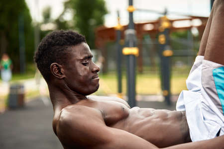 Young black man doing crunches outdoors. He is in a park.の写真素材