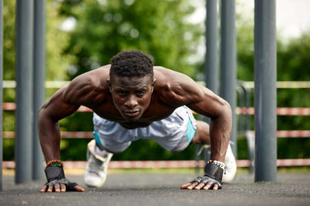 Working out in the morning. Young strong african man in sportswear exercising outdoors. Sport, training concept. Healthy active lifestyle.の写真素材