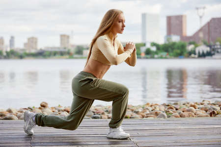 Blonde young athletic woman working out in a park in an urban environment. Attractive athletic woman exercising outdoors in the morning, copy space. Health, fitness conceptの写真素材