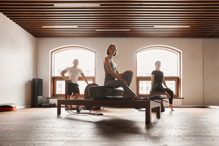 Group of friends doing pilates kneeling glutes exercises on reformer beds in a gym in a health and fitness conceptの写真素材
