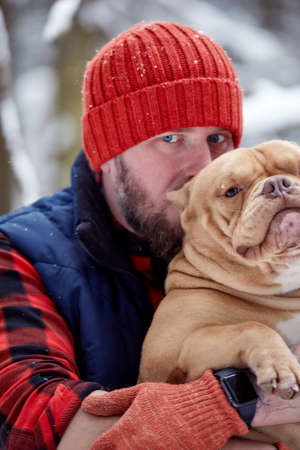 Happy man holding lovely dog in his hands in snowy forest. Smiling boy hugging adorable puppy in winter wood. Pet lover. Dog - human s friend concept.の写真素材