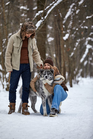 Young couple smiling and having fun in winter park with their husky dog
