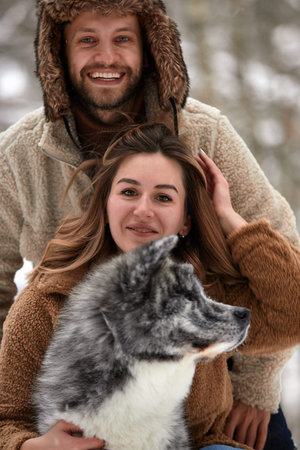 Young couple smiling and having fun in winter park with their husky dog