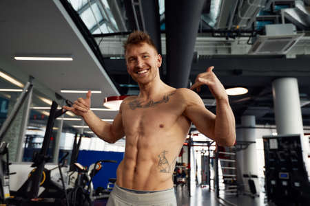 Young handsome sportsman doing exercise at gym shouting with crazy expression doing rock symbol with hands up. Music star. Heavy music concept.の写真素材