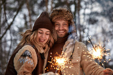 Couple Love Story in Snow Forest Kissing and Holding Sparklers. Couple in Winter Nature. Couple Celebrating. Valentines day date.の写真素材
