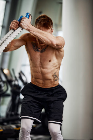 Rear view of Attractive young fit and toned sportswoman working out with battle ropes. Motion blur