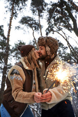 Couple Love Story in Snow Forest Kissing and Holding Sparklers. Couple in Winter Nature. Couple Celebrating. Valentines day date.の写真素材
