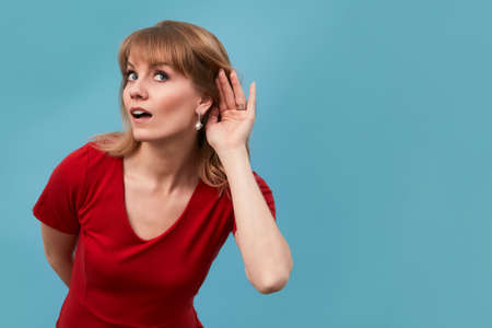 Portrait of an attrative long hair young woman making what did you say sign by putting her hand to her ear wearing red dressの写真素材