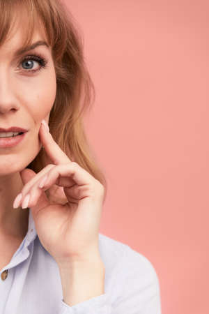 Portrait of a happy smiling mature woman with hand on chin looking at camera. Close up face of beautiful woman with fair hair on rose background. Copy spase for textの写真素材