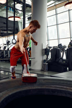 Man fitness training with large and heavy tire hits hammer. Concept workout, cross strengthの写真素材