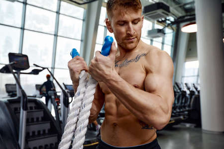 Front view of Attractive young fit and toned sportswoman working out with battle ropes. Motion blurの写真素材