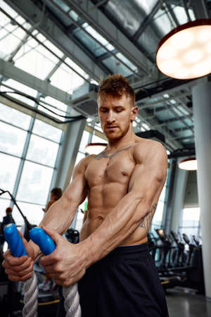 Muscular powerful aggressive man training with rope in functional training fitness gym. Motion blurの写真素材