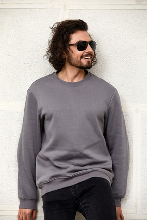 Fashion portrait of handsome elegant man with curly hair wearing gray sweater and glasses on gray...