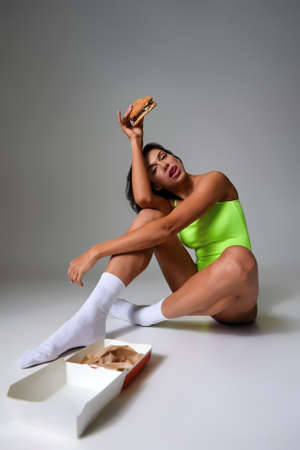 Sexy athletic woman eating hamburger on gray backgroundの写真素材