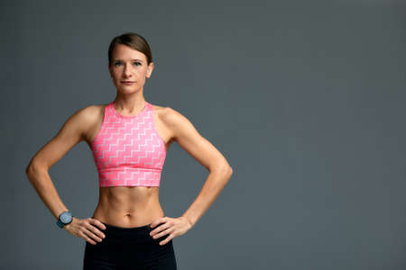 Smiling attractive young fitness sporty woman 20s wearing sportswear posing working out training holding hands on her waist background studio portraitの写真素材