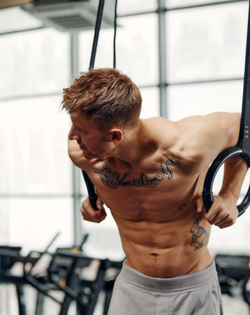 Muscle-up exercise young man doing intense cross fit workout at the gym on gymnastic rings.