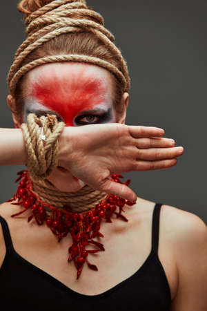 close up portrait of young beautiful girl with colorful face painting. Halloween professional makeup. hair in paint. neck and hands are wrapped with ropes. Victim Conceptの写真素材