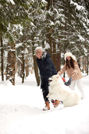 Family of mother, father and son having fun in snowy winter wood with cheerfull pet dog.の写真素材