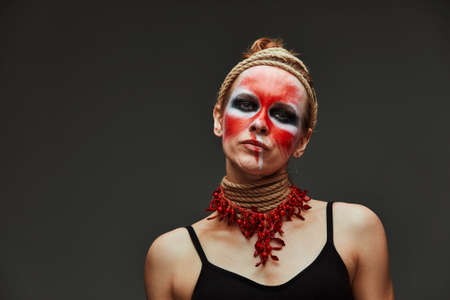 close up portrait of young beautiful girl with colorful face painting. Halloween professional makeup. hair in paint. neck and hands are wrapped with ropes. Victim Conceptの写真素材