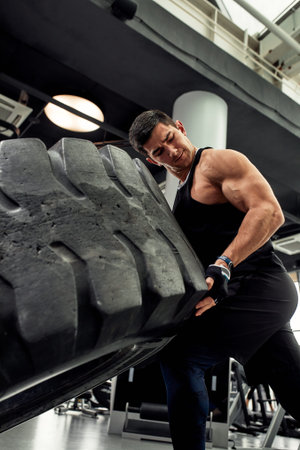 Muscular fitness man flipping tire wheel. Concept functional training workout gym