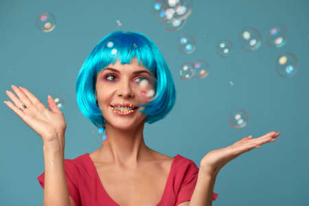 Beautiful young woman with blue wig and bright make-up in soap bubbles. Fashion model girl with creative color makeup. Women doll concept.の写真素材