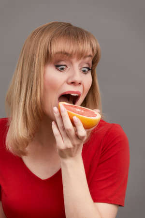Closeup of extremely joyful adult woman holding grapefruit with great happiness, having big desire to eat delicious sugary sweet food. indoor studio shot isolatedの写真素材