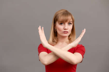 Woman making stop sign with crossed hands. Serious girl denying, refusing any action, looking at camera on gray background.の写真素材