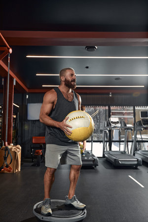 The guys tries to keep his balance on the balancing platform with fitness ball. Group exercise with the help of a fitness trainer.の写真素材