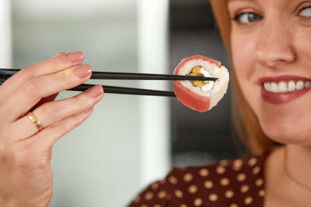 Attractive woman resting at home with sushi. Eating sushi with chopsticks close up, food takeout and delivery service, salmon sushi rolls, tasty meal, sushi deliveryの写真素材
