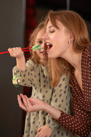 Little girl feeding her mother sushi with chopsticks close up. Food takeout and delivery service,...