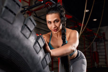 Fit female athlete working out with a huge tire, turning and flipping in the gym. Crossfit woman...