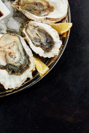 Oysters with lemon served on black round platter. Luxury delicatessen seafood.