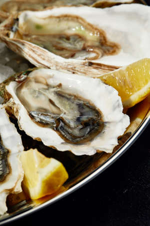 Oysters with lemon served on black round platter. Luxury delicatessen seafood.の写真素材