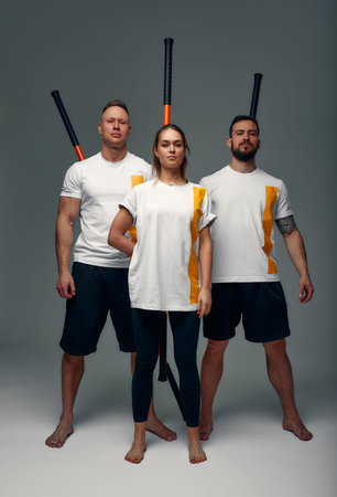 Two men and woman aikido fighters with wooden fight stick posing in studio, fight demonstration
