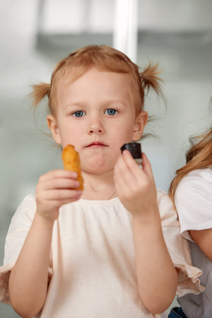 Cute smiling little girl with sushi on white background. Child girl eating sushi and rolls -...