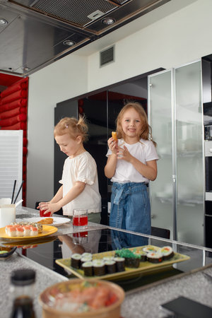 Two little girls siblings having fun and eating on the kitchen at home with japanese food.の写真素材
