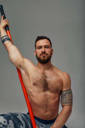 A ninja man holds on to a fighting stick and attacks close-up on gray studio backgroundの写真素材