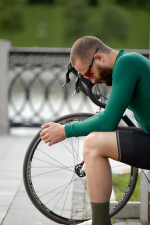 Stylish handsome guy cyclist rests on a wooden bench near bicycle in summer park.の写真素材