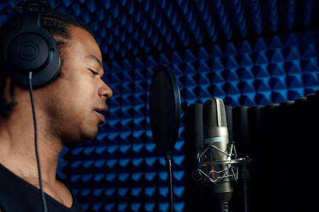 Close-up of handsome young Black singer standing in front of microphone singing song in recording studioの写真素材