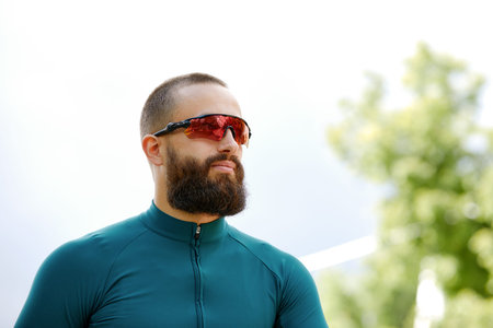 Close up shot of happy attractive young European man with beard wearing glasses and green sportswear...