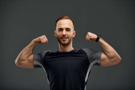 Portrait of a handsome young guy model with hairstyle in a trendy black tank top mock up with a muscular healthy body showing off his biceps muscles on a gray backgroundの写真素材