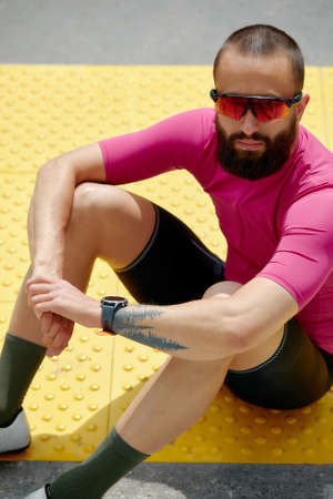 Portrait of a smiling fitness man resting while sitting on a ground at the track field outdoorsの写真素材