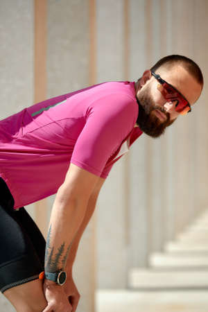 Close up shot of happy attractive young European man with beard wearing glasses and pink sportswear looking at camera during evening ride in park on weekend.の写真素材