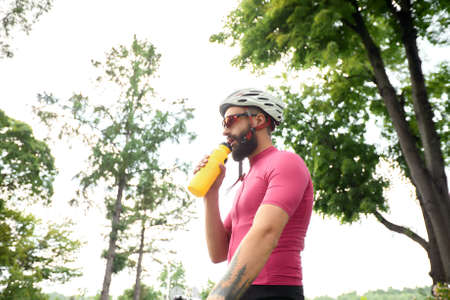 Strong Male cyclist in sportswear, glasses and protective helmet walking with his bike in the forest to take a break after riding. Sky blue and forest in the background.の写真素材