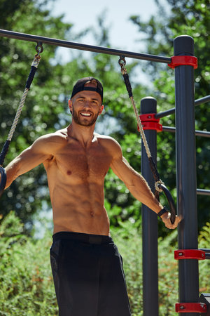 Young man exercising in an outdoor bodybuilding gym using gymnastic rings