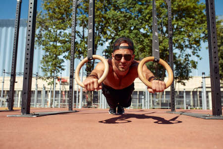 Muscular sportsman exercising on outdoor gymnastic rings in outdoor gym. Hands at rings dipping man doing exercise using ringsの写真素材