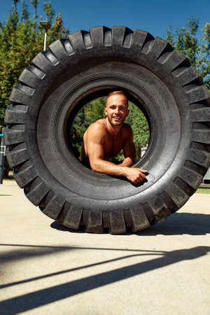 Strong man training workout lifting large tire outdoor gym. Sportive young adult caucasian guy flip big wheel on nature. Handmade equipment sport exercising helthy lifestyle conceptの写真素材