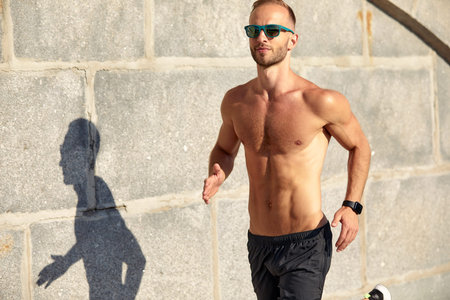 Urban sports. Sporty man shirtless jogging for fitness in the city park on a beautiful summer day